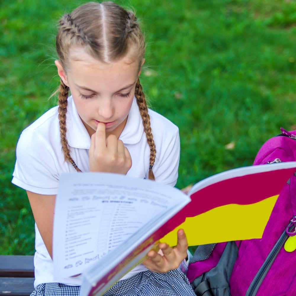 School-age girl reading while biting on her finger nails