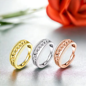 Gold, silver and rose gold fidget ringson a shiny surface with a red rose in background
