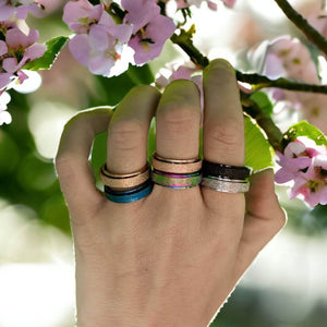 Woman's hand wearing six multi coloured anxiety rings on a cherry blossom background