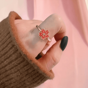 Woman's hand wearing a flower ring with spinning top on the index finger on pink background