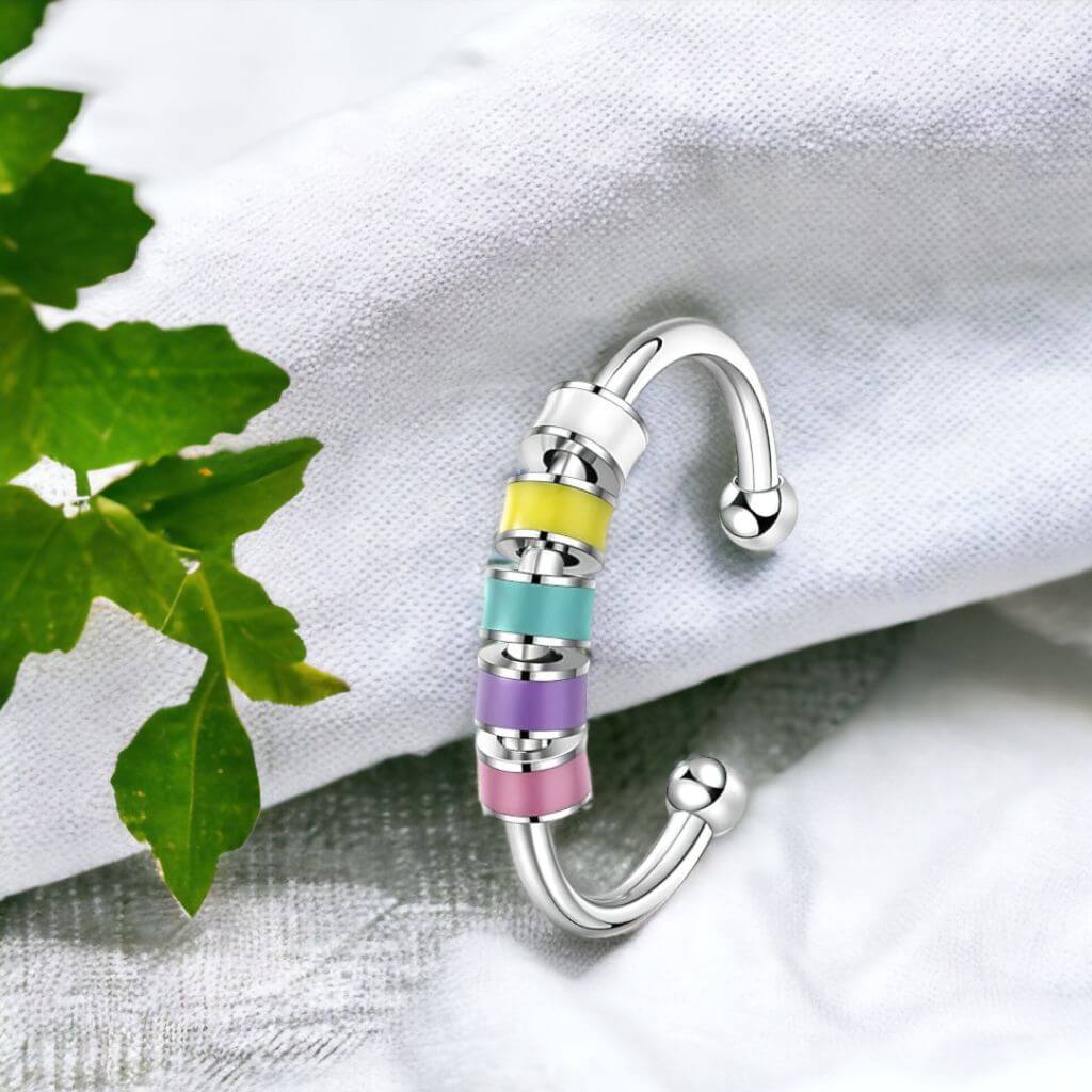 Adjustable ring for fidgeting with enamel beads on grey fabric next to a green plant