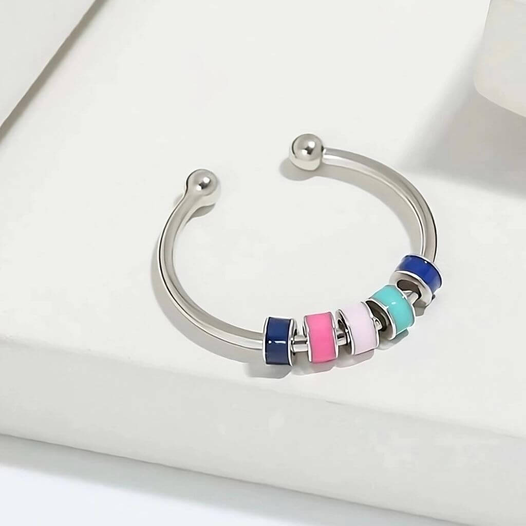 Adjustable ring for fidgeting with enamel beads on a white podium