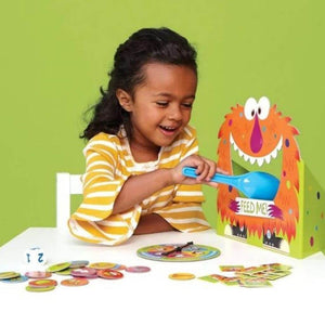 Afro american girl playing Feed the Woozle cooperative board game at a white table on green background