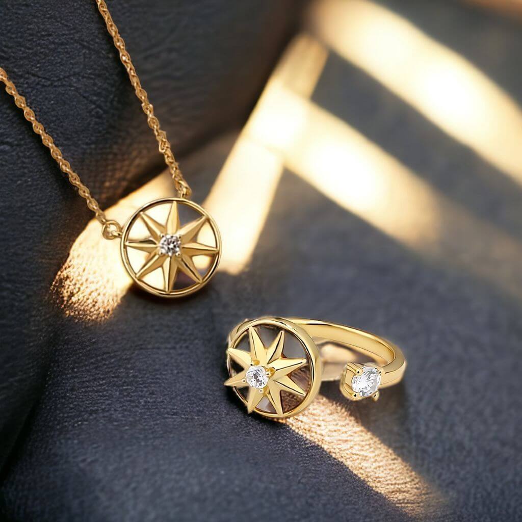 Gold-toned jewelry set featuring a necklace and matching ring, both with a circular compass-like star motif and small clear stones, displayed on a dark textured surface with warm sunlight shadows.