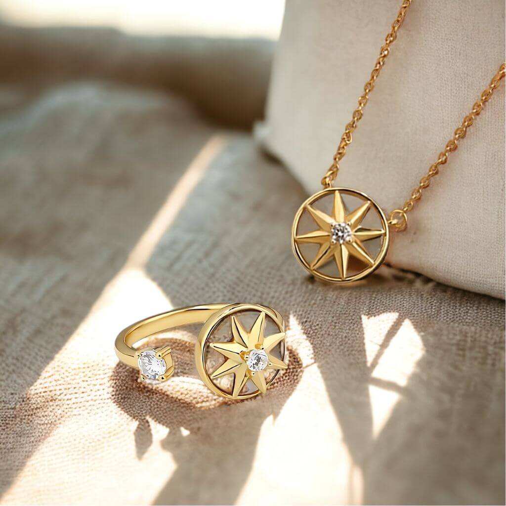 Gold-toned jewelry set featuring a compass rose pendant necklace on a chain and a matching ring, both adorned with small clear stones, displayed on a textured beige fabric surface.