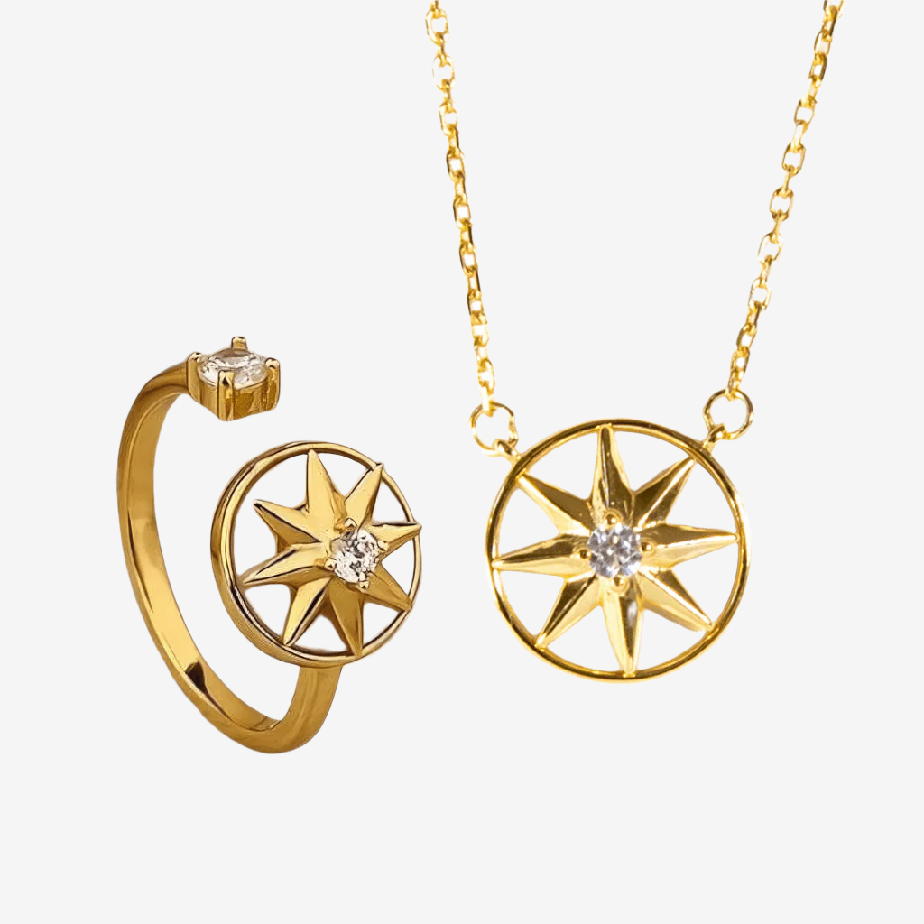 Gold jewelry set featuring a compass rose pendant necklace and a matching open-band ring, both with a central clear gemstone, on a light gray background.