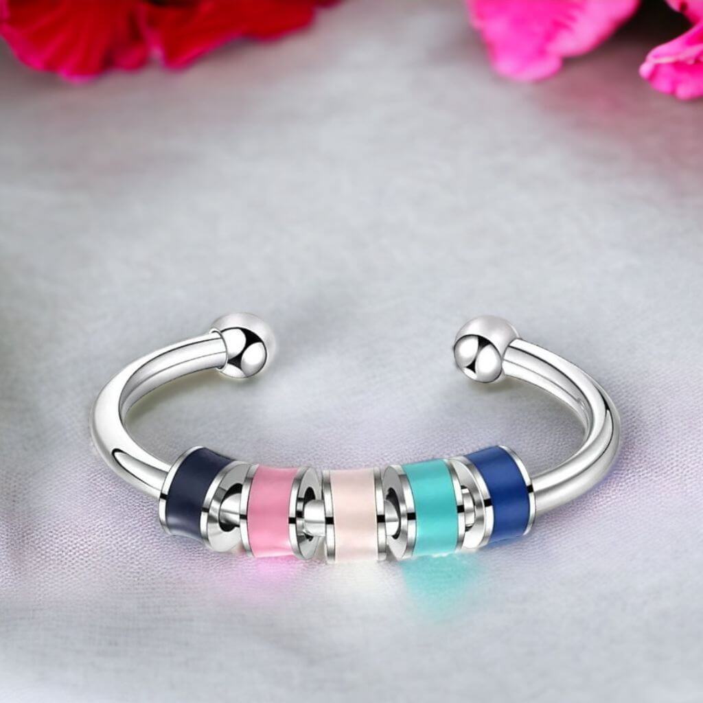 Anxiety ring with enamel beads on a light grey surface and pink flowers