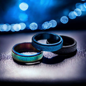 Black, blue and rainbow anxiety rings on a black surface with blue lights on background