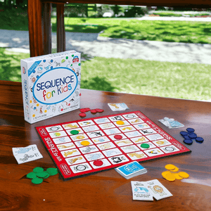 Box and contents of the Sequence for Kids Board Game on a wooden table on grassy background
