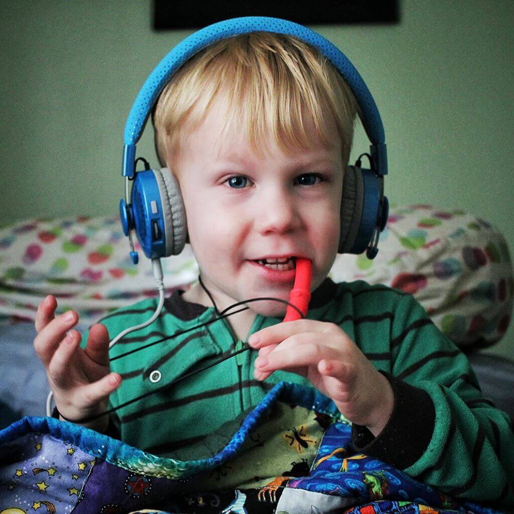 Boy wearing ear muffs chewing  a red bite saber chewing necklace