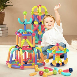 Boy playing with magnetic blocks on the floor surrounded by magnetic balls and sticks constructions 