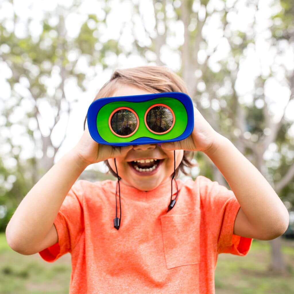 Caucasian boy in orange t-shirt looking through GeoSafari Kidnoculars by Educational Insights in a park
