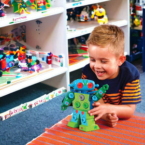 Caucasian boy playing with a Design and Drill Robot by Educational Insights on the floor in a toy store