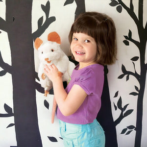 Caucasian girl holding a white mouse puppet from Folkmanis with trees wallpaper in background