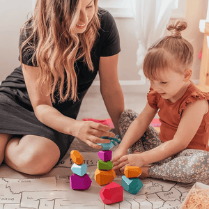 Caucasian mother and daughter playing with colorful stacking stones on the floor