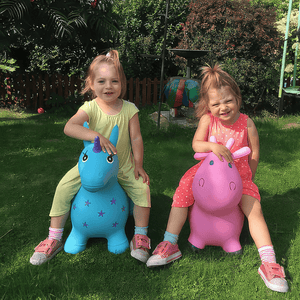 Caucazian toddler girls riding Happy Hopperz Turquoise Unicorn and Pink Cow animal hoppers in the garden