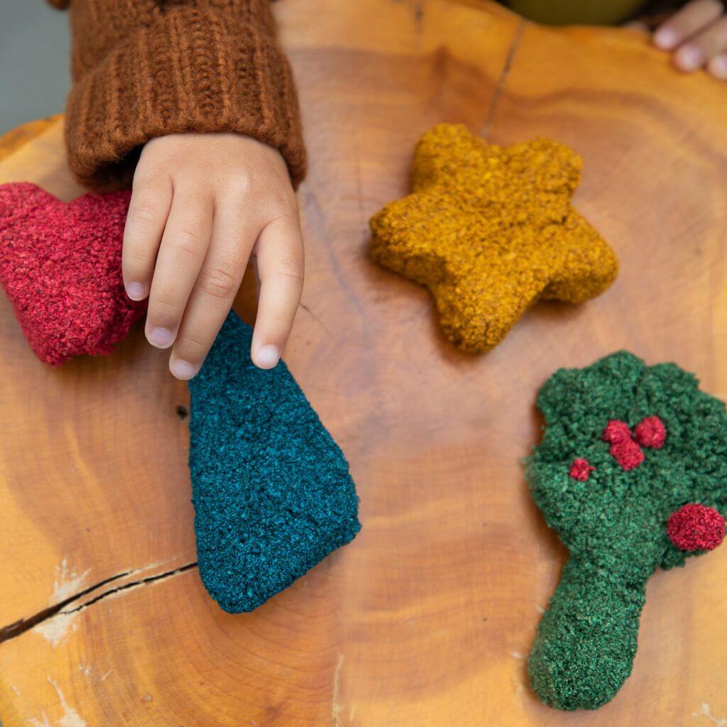 Child's hand making shapes with layfoam® Naturals by Educational Insights at a wooden table