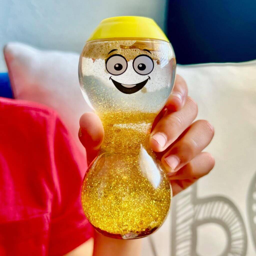 Close up of the yellow Express Your Feelings Sensory Bottle by hand2mind held by a person in red t shirt