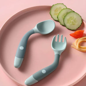 Flexible spoon and fork blue green on a pink silicone plate next to cucumbers and pasta