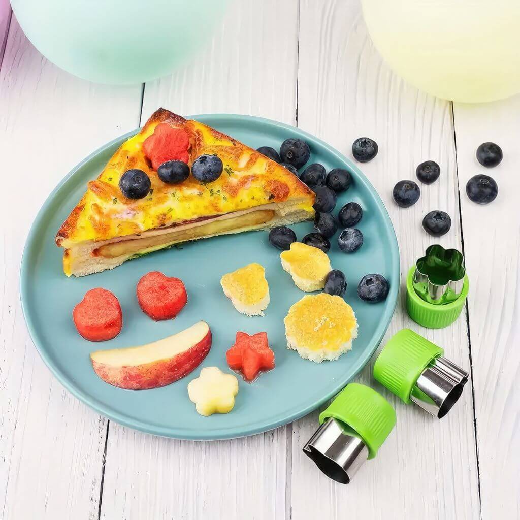 Food cutters, fruits, vegetables and a sandwich on a plate