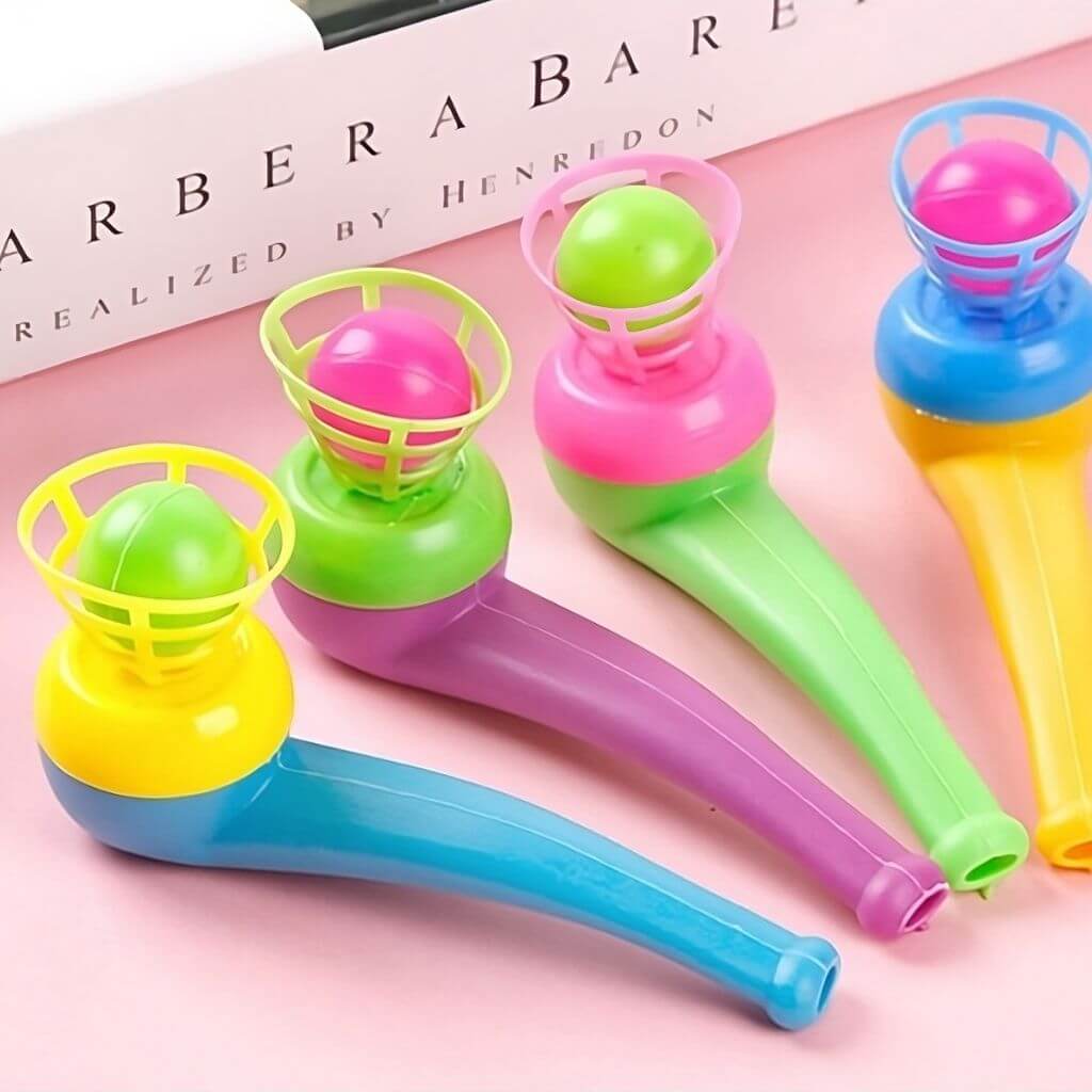 Four multi colored magic ball blow pipes next to a book on a pink background