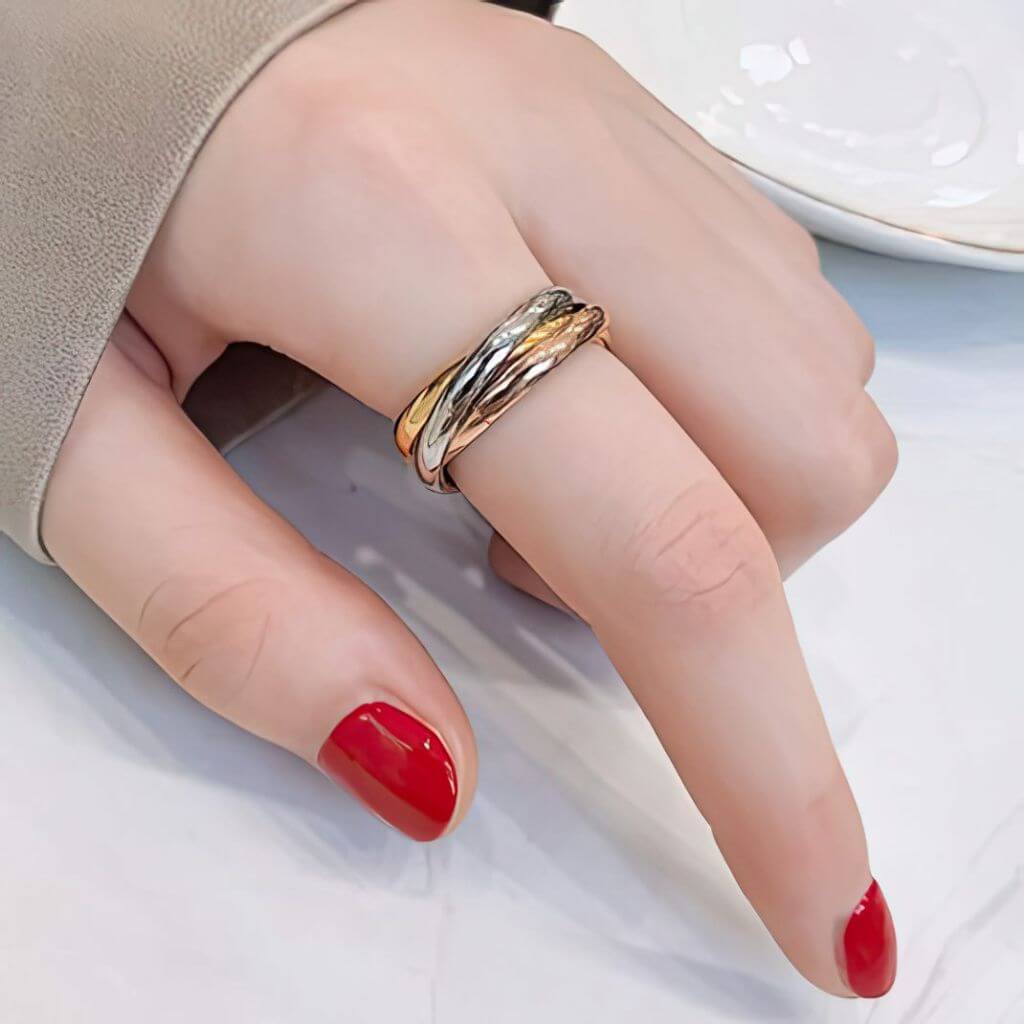 Hand wearing a gold fidget ring with red nail polish on a neutral background
