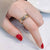 Hand wearing a gold fidget ring with red nail polish on a neutral background