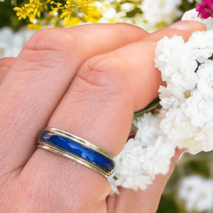 Hand wearing a mood ring holding a white flower