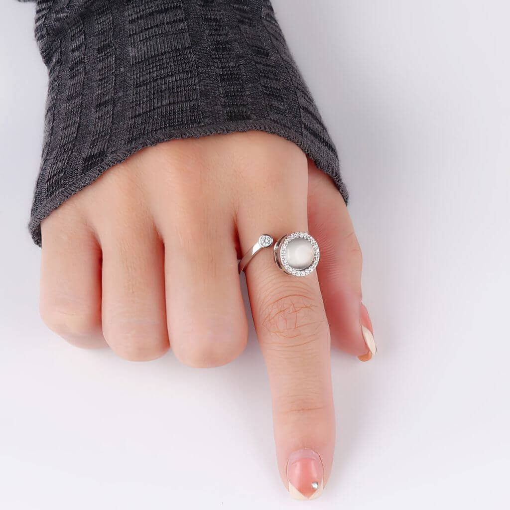 Hand wearing a ring with an opal gemstone center on a white background