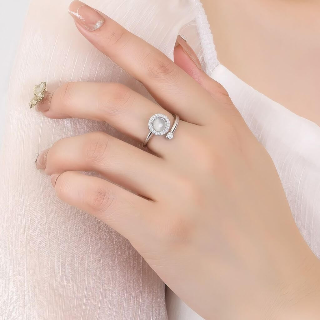 Hand wearing a silver ring with an opal center on a light background