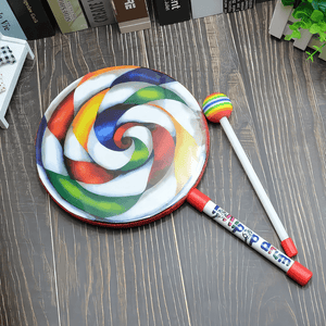 Lollipop drum and beater on a wooden table with books in background