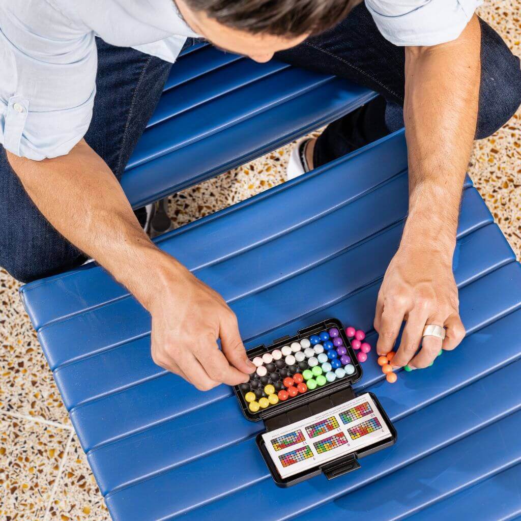 Man playing Kanoodle puzzle game on a blue chair