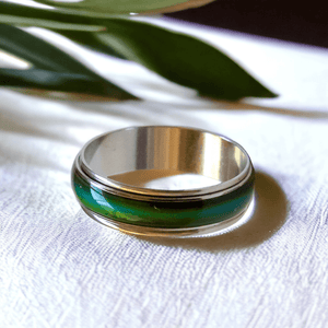 Mood ring with green band next to a green leaf on a white surface