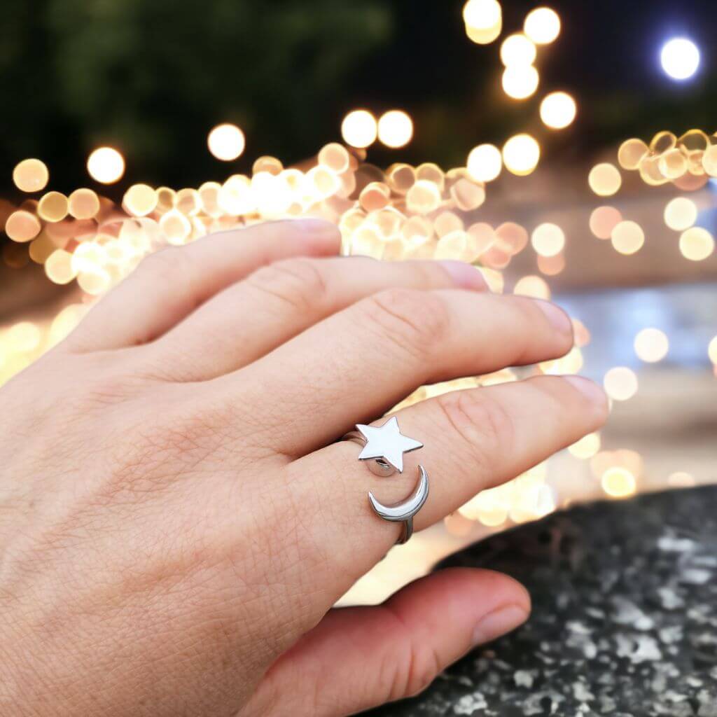 Moon and star anxiety ring adjustable on an index finger with a blurry night background
