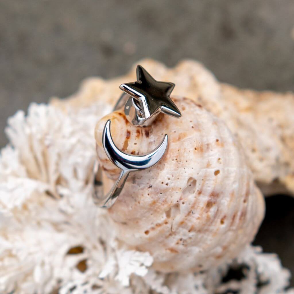 Moon and star spinning ring on a sea shell next to seaweed on sand 