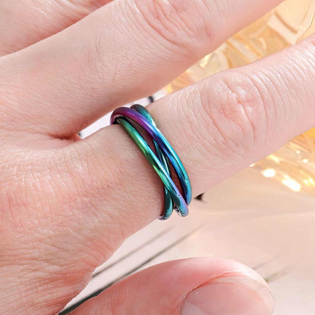 Four stainless steel fidget rings in different colors on a white background