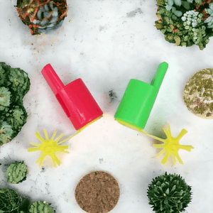 Red and green propeller whistles on a marble counter top surrounded by succulents