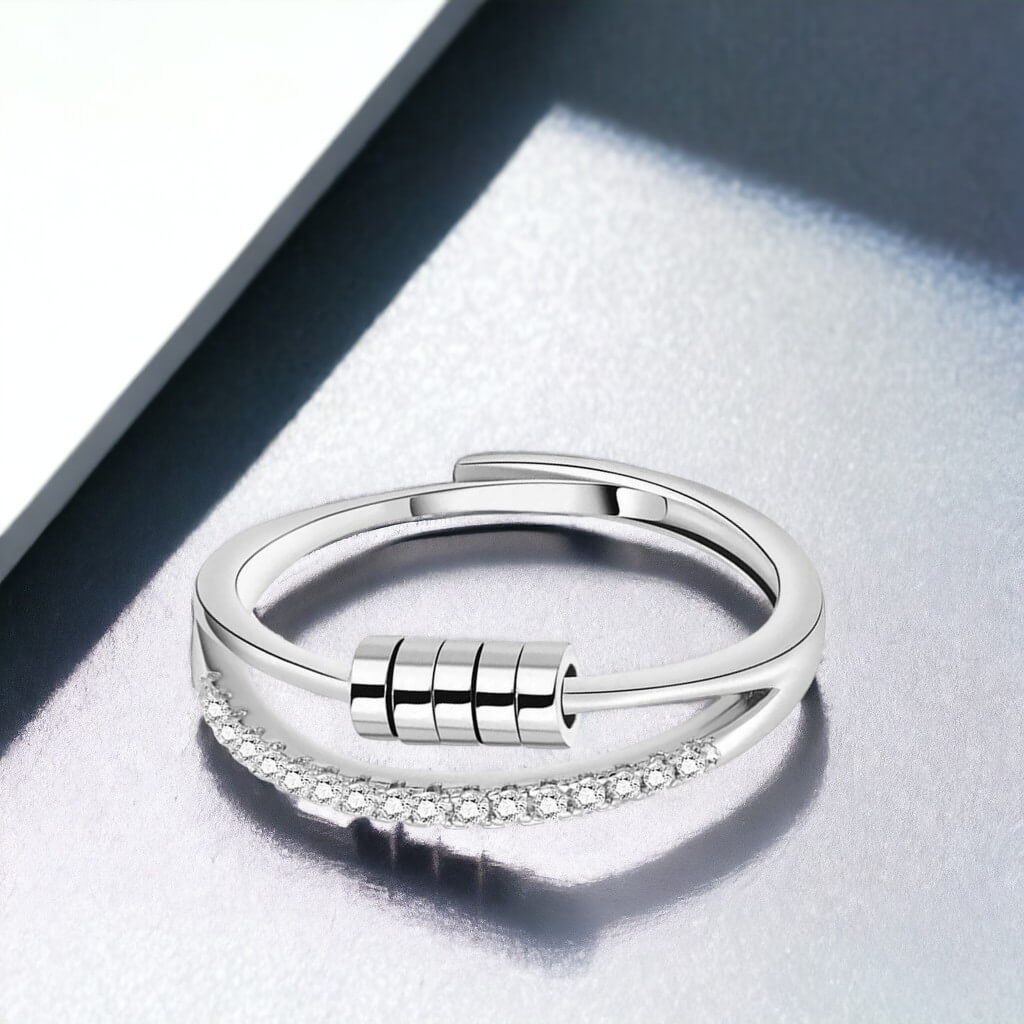 Silver anti anxiety ring with cubic zirconia and sliding beads on a grey surface