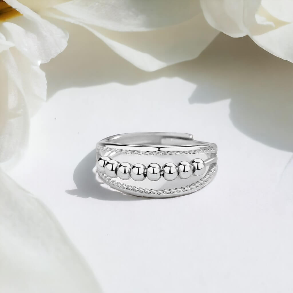Silver fidget ring on a white surface with white flowers in background
