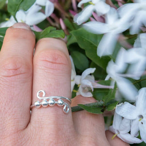 Silver ring on a finger with white flowers and green leaves in the background