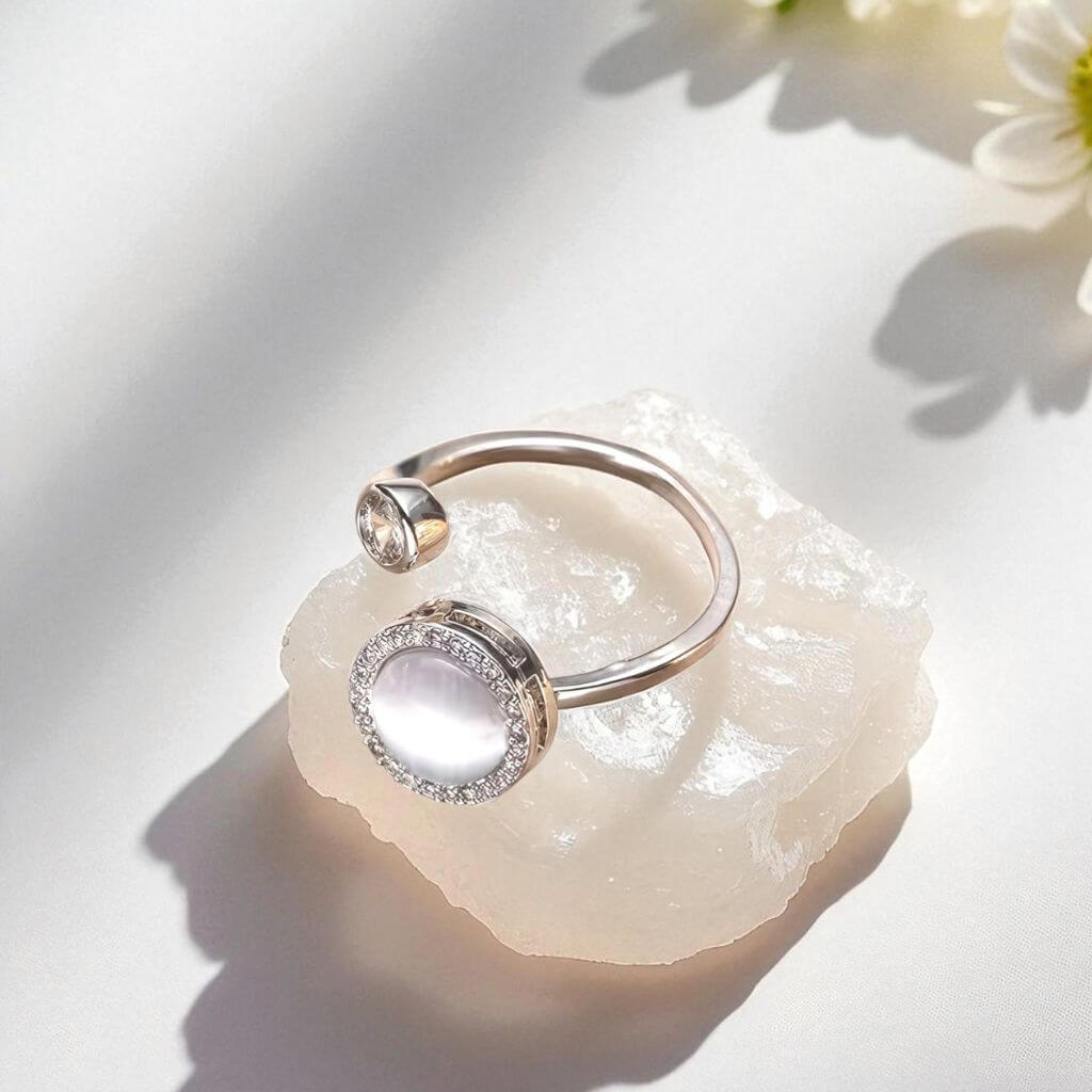 Silver ring with an opal gemstone on a light stone surface with flowers in the background
