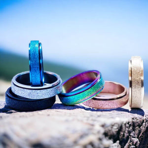 Six multi coloured fidget rings on a grey stone with blue sky on background