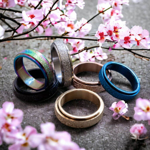 Six multi coloured fidgeting rings on a grey surface with a cherry blossoms in background