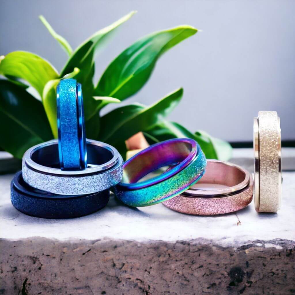 Six multi coloured spinning rings on a grey counter top with a green plant on background