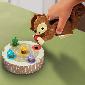 Child's hand holding a squirrel, next to acorns and log from the Sneaky Snacky Squirrel Game on a green surface 