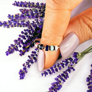 Stainless steel adjustable spinning ring with  enamel beads on an index finger next to lavender flowers