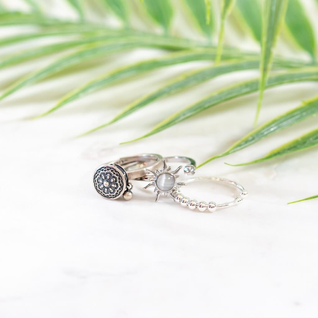 Three spinner rings silver on a white surface with a palm leaf background
