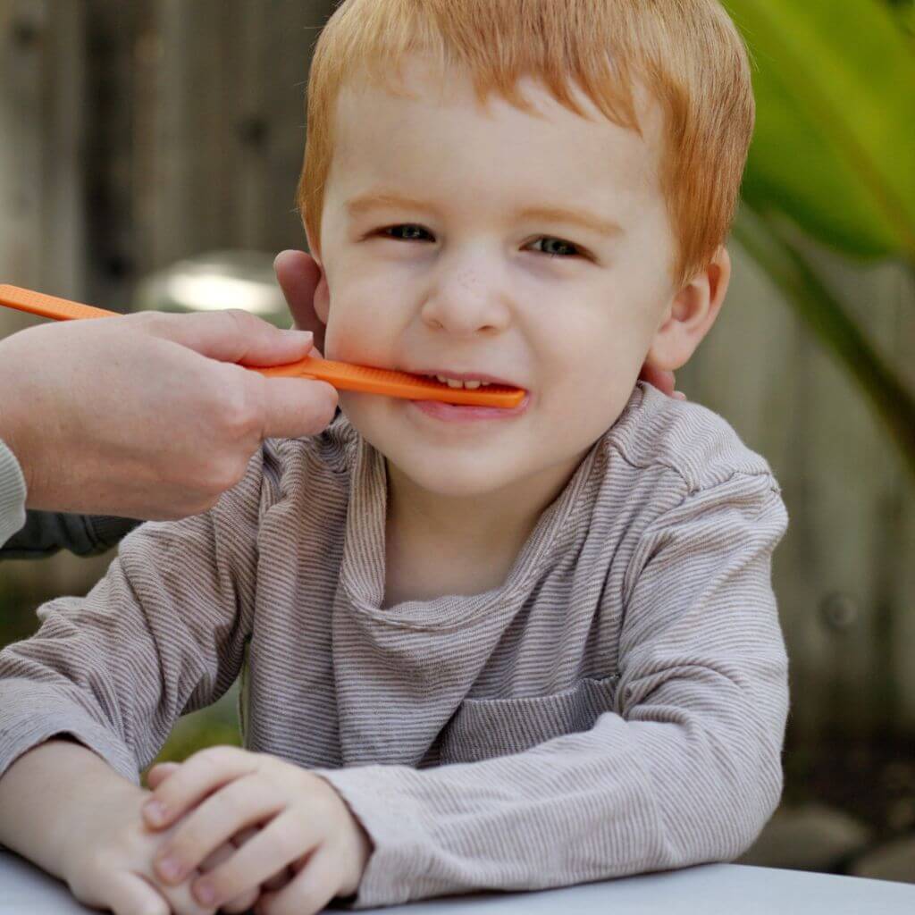 Toddler boy biting an orange bite block from Ark Therapeutic