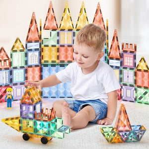 Toddler boy playing on the floor with a car made of pastel magnetic tiles with a castle on background
