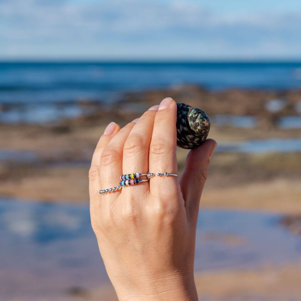 Woman's hand holding a shell wearing 3 anxiety rings in Australia sea 